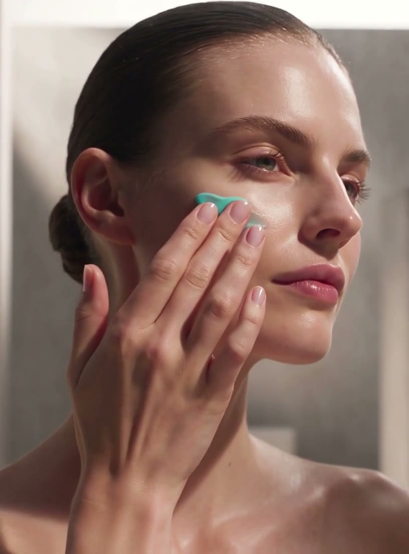 A woman smoothing cobalt-blue cream onto her cheek with her fingertips.